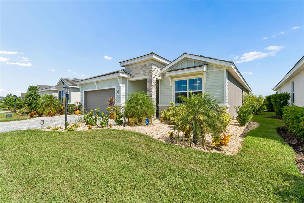 A single-story house with light green siding, a stone facade, and a paved driveway — 18123 GULF RANCH PLACE, LAKEWOOD RANCH, FL