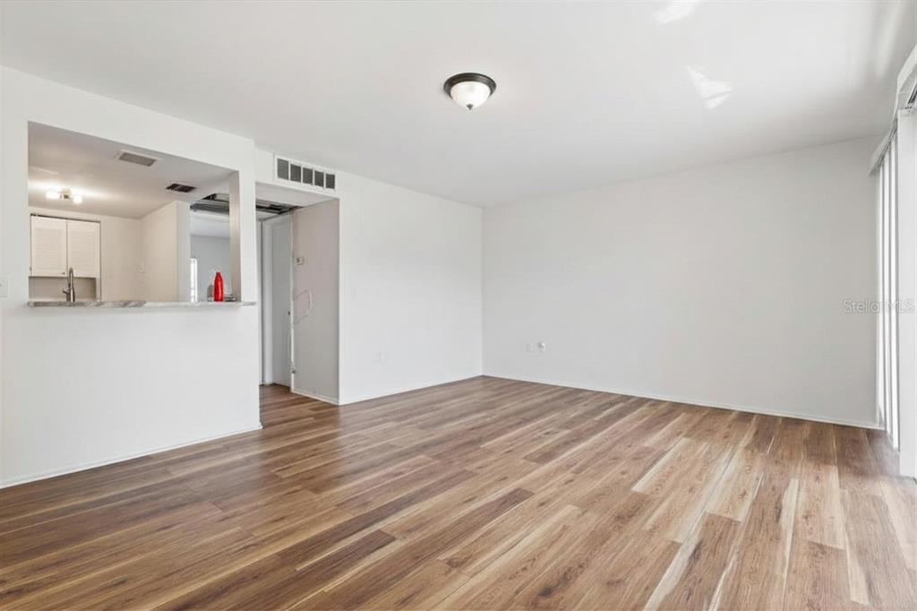 An empty living room features wood-look flooring, white walls, and an open kitchen pass-through — 3840 N LAKE DRIVE UNIT 125, TAMPA, FL