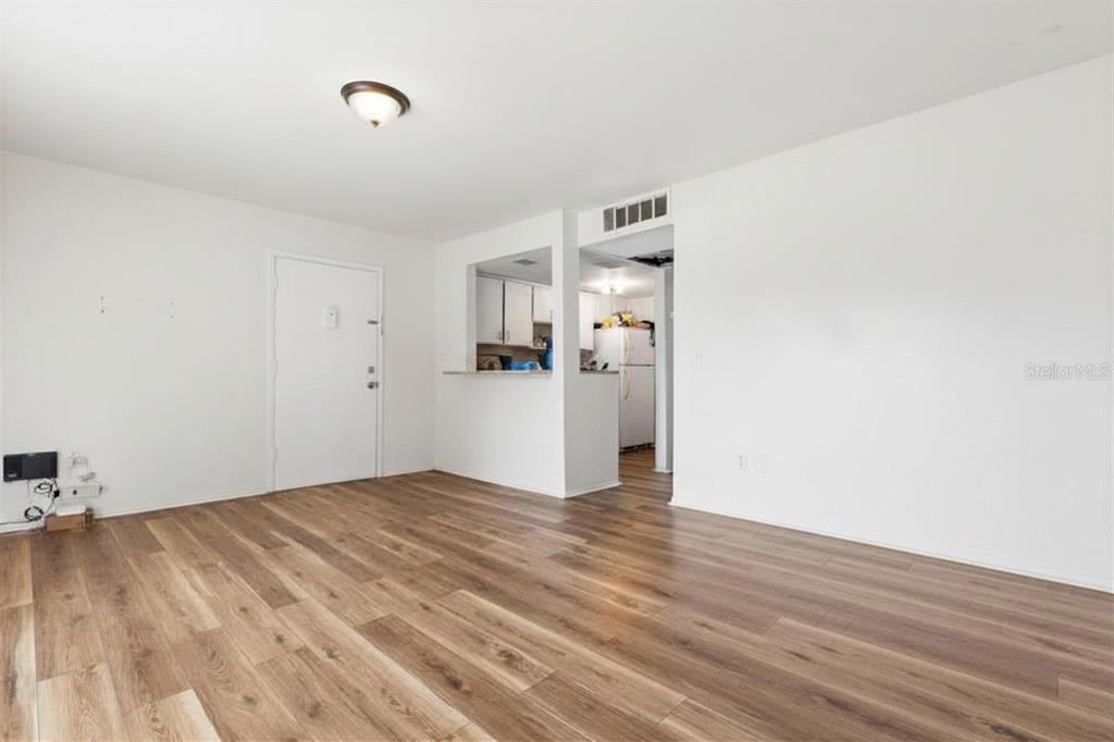 An empty room with light wood-look flooring and a pass-through opening to the kitchen — 3840 N LAKE DRIVE UNIT 125, TAMPA, FL