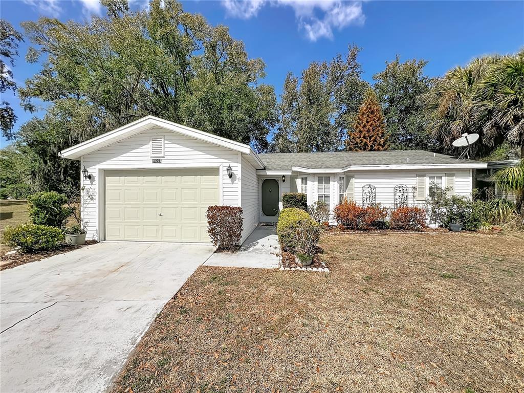 A single-story white house with a garage, concrete driveway, and landscaping under a blue sky — 25227 WILD HERON, LEESBURG, FL