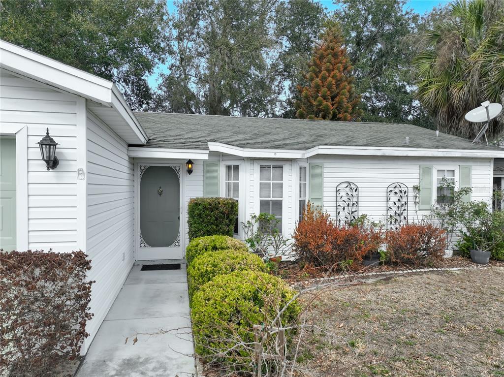 The exterior of a white, single-story house features a front door, walkway, and landscaping — 25227 WILD HERON, LEESBURG, FL