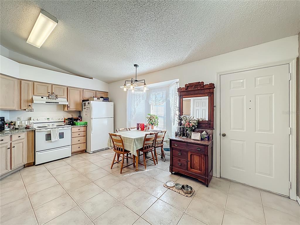 A kitchen with light wood cabinets, white appliances, tile flooring, and a dining area — 25227 WILD HERON, LEESBURG, FL
