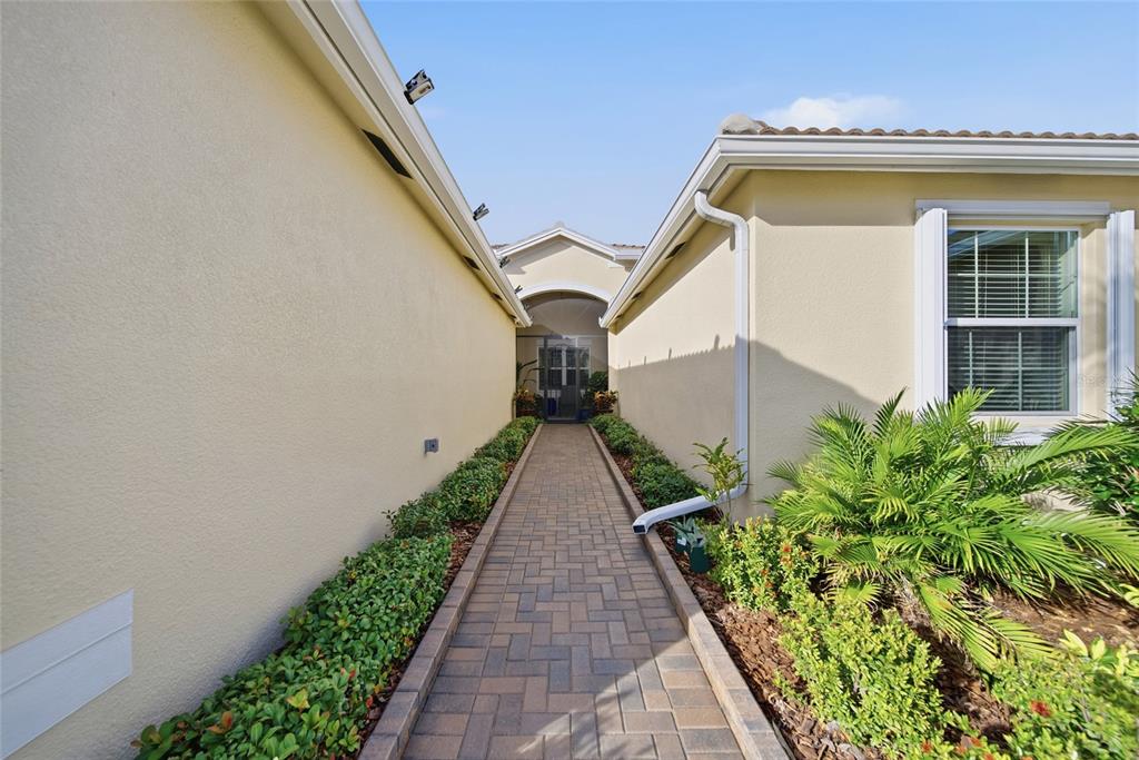 A paved walkway leads between two beige exterior walls toward a screened entryway — 4717 AVILA LAKES DRIVE, WIMAUMA, FL