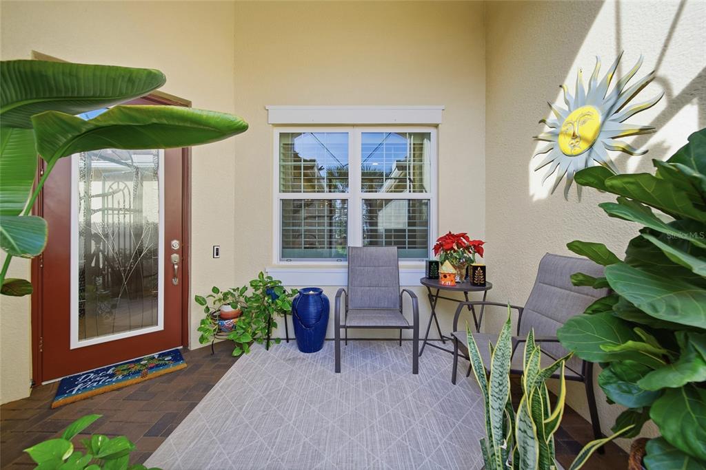 A covered patio features a patterned rug, two chairs, a small table, and potted plants — 4717 AVILA LAKES DRIVE, WIMAUMA, FL