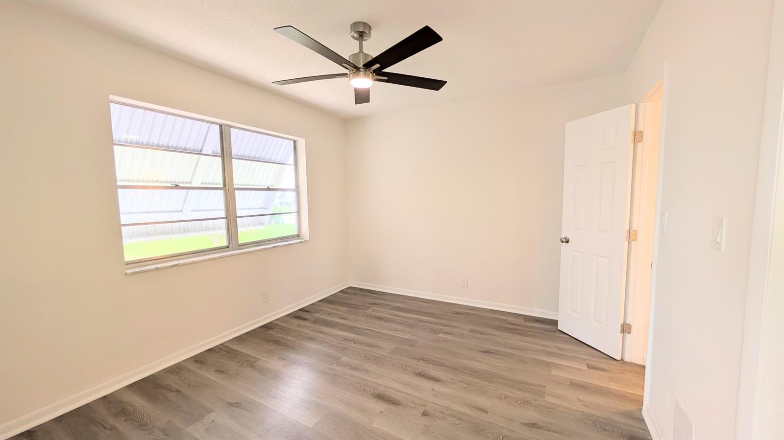 An empty bedroom features light-colored walls, wood-look flooring, a ceiling fan, and a window — 2800 W Golf Boulevard # 219, Pompano Beach FL 33064, POMPANO BEACH, FL