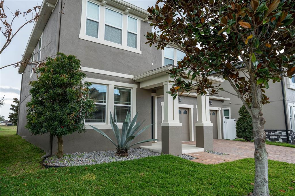 A two-story house exterior with a gray stucco facade, a covered porch, and a brick driveway — 2963 SERA BELLA WAY, KISSIMMEE, FL