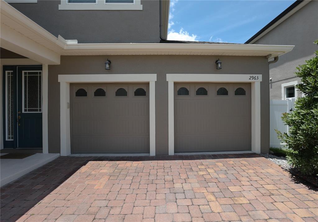 A two-car garage with brown doors and arched windows sits beside a paved driveway — 2963 SERA BELLA WAY, KISSIMMEE, FL