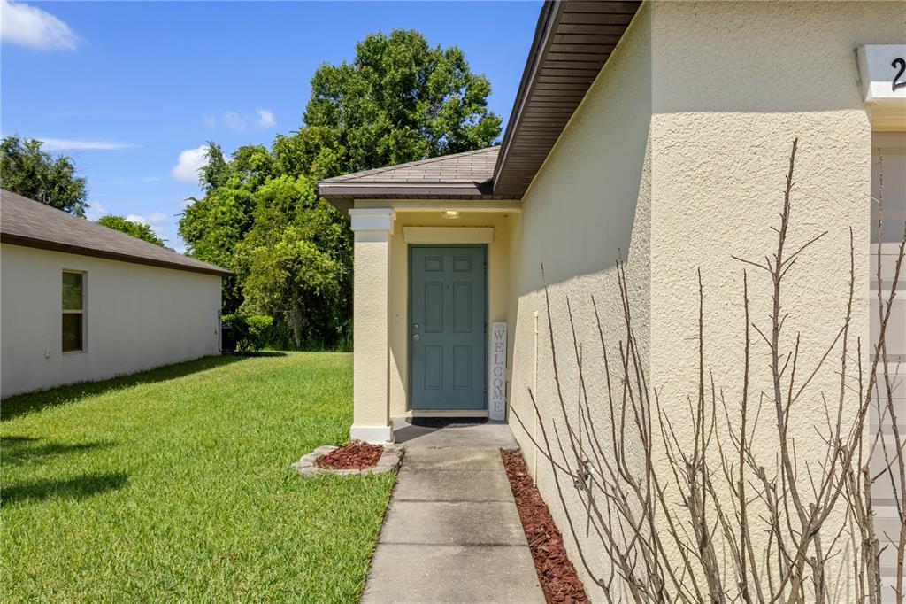 A concrete walkway leads to a blue front door on a light-colored stucco house — 2987 MOULDEN HOLLOW DRIVE, ZEPHYRHILLS, FL