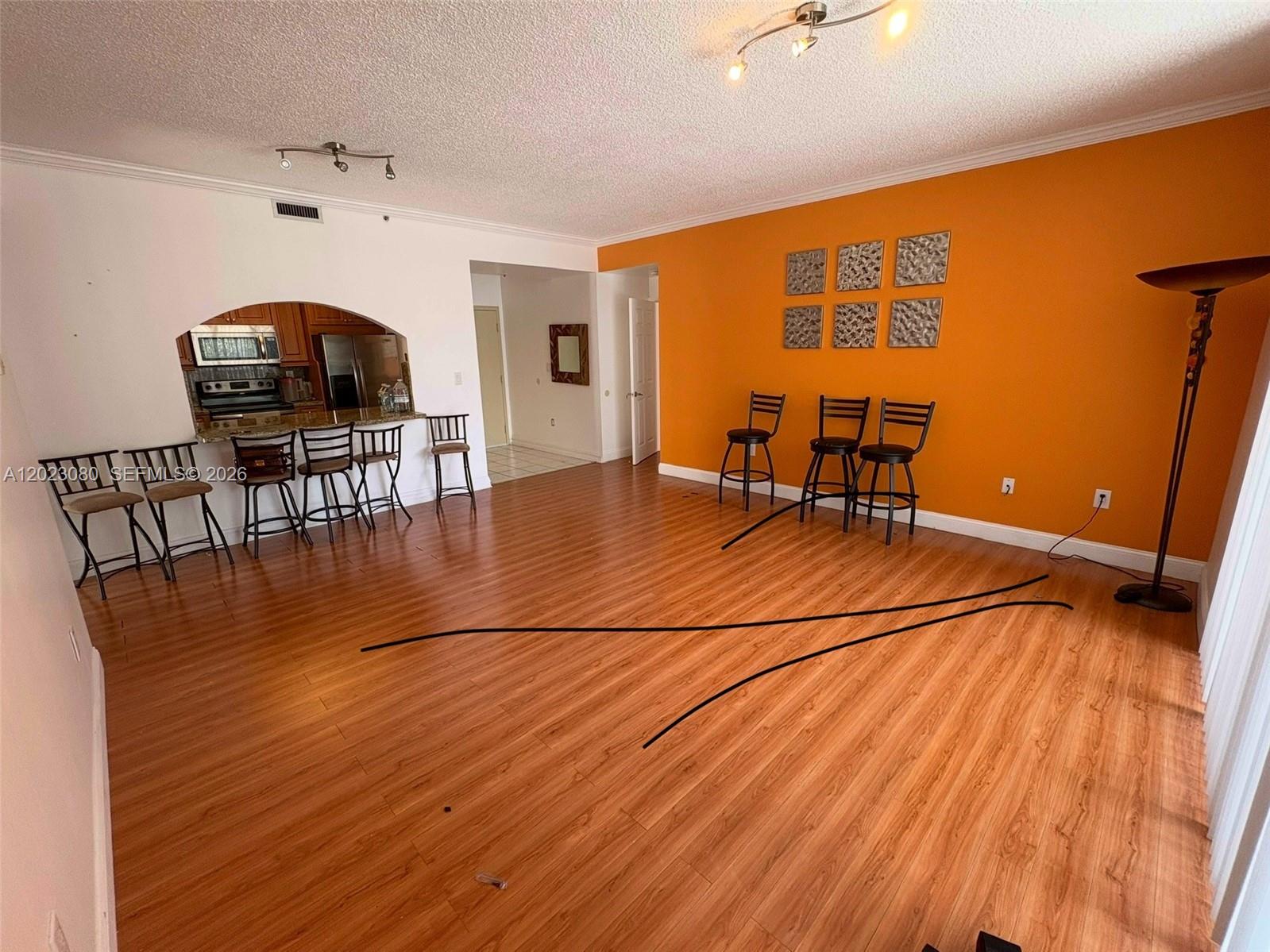 An empty room features dark wood-look flooring, a textured ceiling, and sliding glass balcony doors — DORAL, FL
