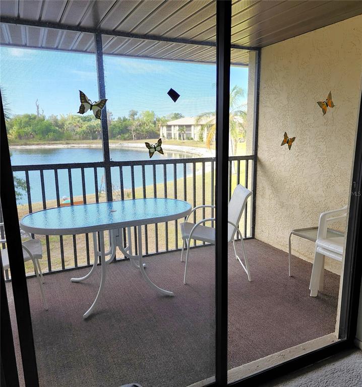 A screened-in balcony features a glass-top table, chairs, and a view of a lake — 4056 OAKVIEW DRIVE UNIT E10, PORT CHARLOTTE, FL
