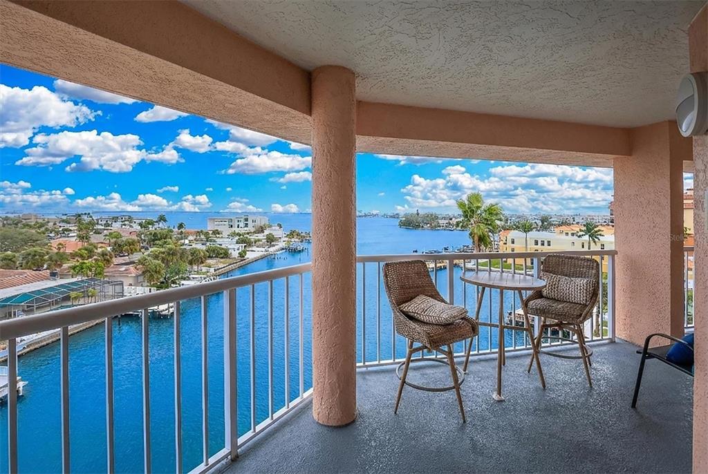 A balcony with wicker chairs and a table overlooks a canal and coastal buildings — 5445 GULF BOULEVARD UNIT PH1, ST PETE BEACH, FL
