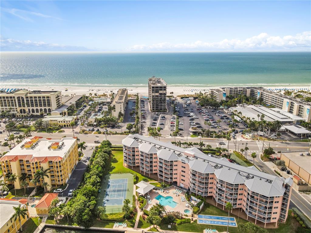 An aerial view of a coastal resort featuring multi-story buildings, a tennis court, and pool — 5445 GULF BOULEVARD UNIT PH1, ST PETE BEACH, FL