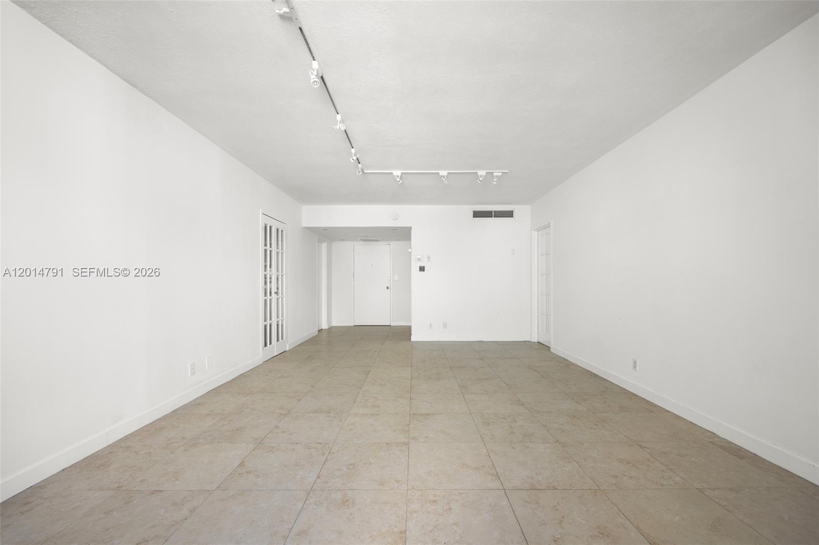 An empty room features white walls, tile flooring, and a ceiling-mounted track lighting system — 900 Bay Dr # 1005, Miami Beach FL 33141, MIAMI BEACH, FL