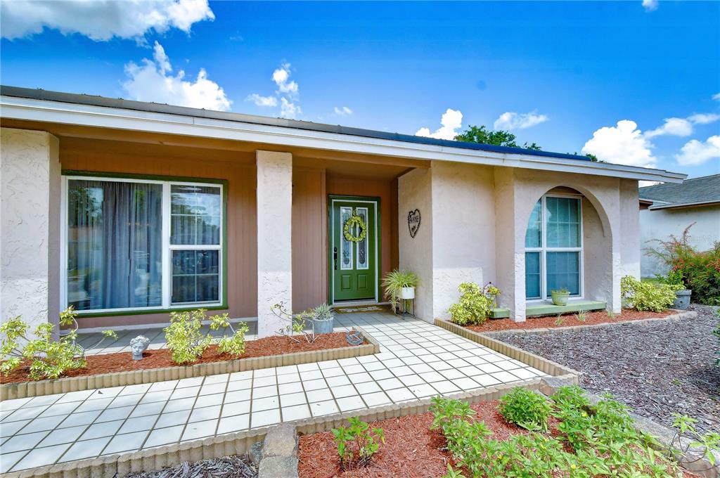 A single-story house exterior features a green front door, tiled walkway, and arched window — 12604 TRUCIOUS PLACE, TAMPA, FL