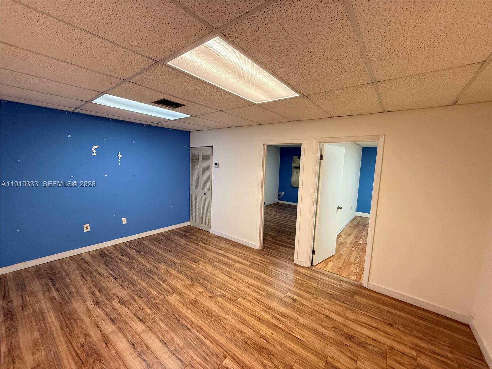 An empty room features blue and white walls, wood-look flooring, and a drop ceiling — 8000 NW 31st St # 19, Doral FL 33122, DORAL, FL