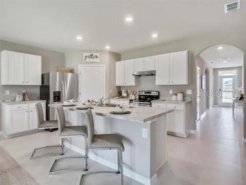 A kitchen features white cabinets, stainless steel appliances, a granite island, and gray bar stools — 679 MADRID DRIVE, KISSIMMEE, FL
