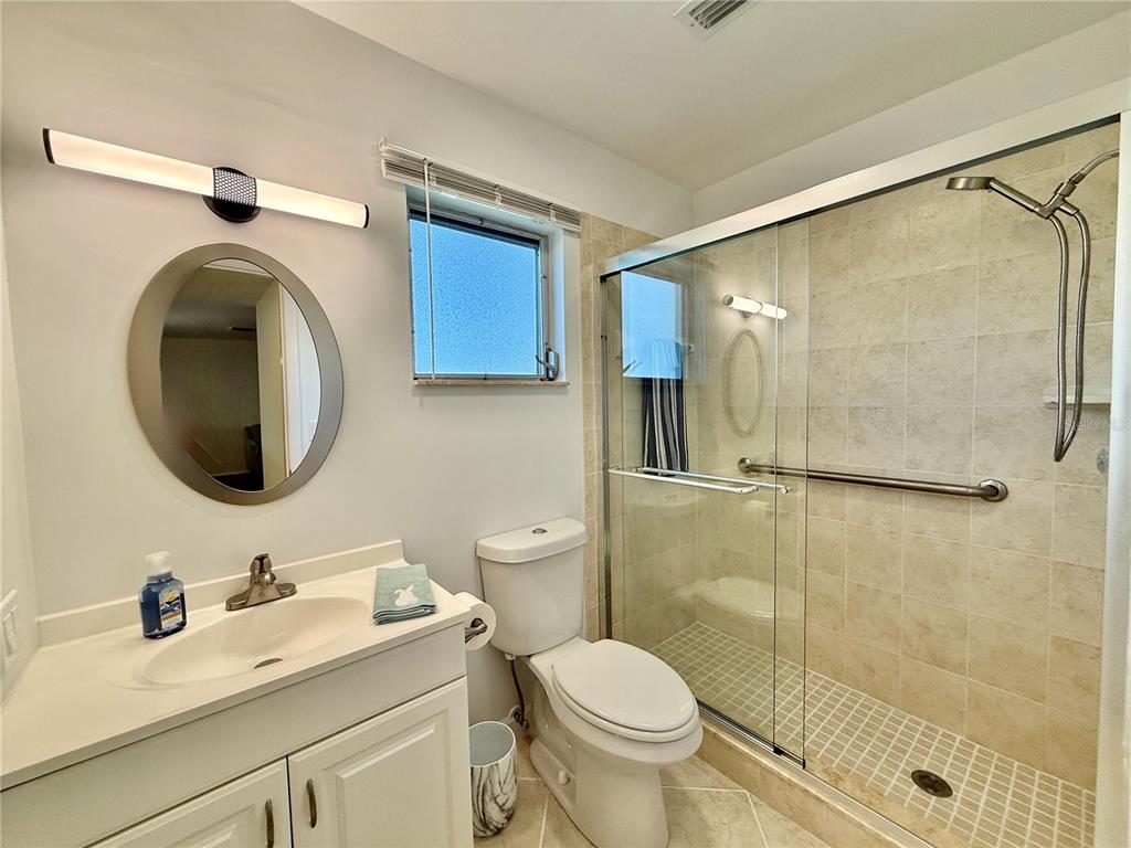 A bathroom features a white vanity, a round mirror, a toilet, and a tiled shower — 2221 ORANGE BLOSSOM LANE, BRADENTON, FL
