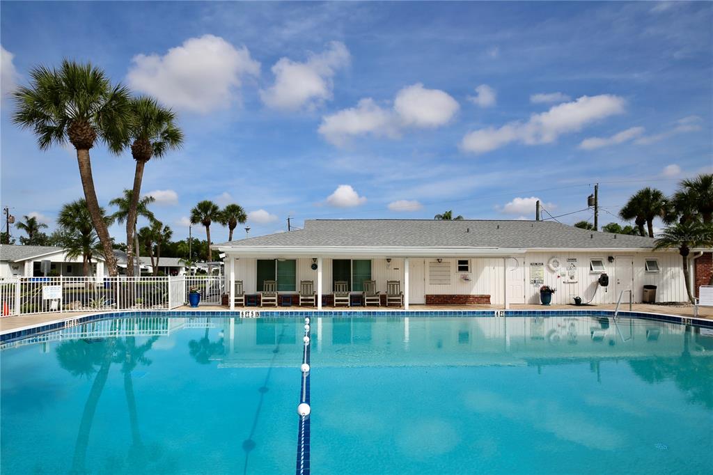 A swimming pool sits in front of a white building with palm trees under a sky — 2221 ORANGE BLOSSOM LANE, BRADENTON, FL