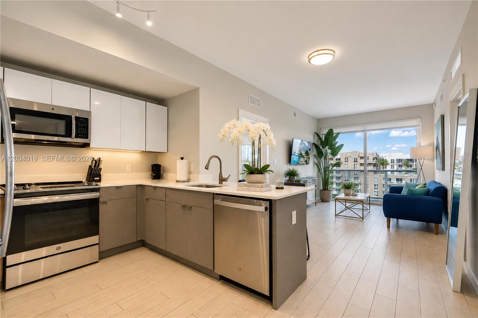 A modern kitchen with stainless steel appliances and gray cabinets opens to a living area — 321 NE 26th St # 806, Miami FL 33137, MIAMI, FL