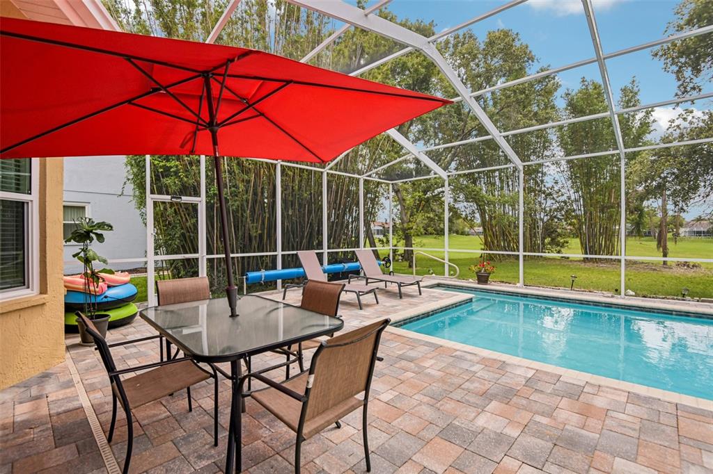 A screened-in patio features a pool, dining set with a red umbrella, and lounge chairs — 14337 BRONTE COURT, HUDSON, FL