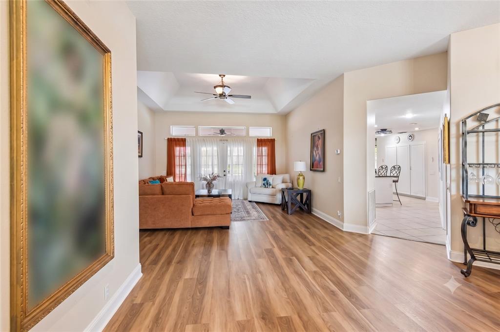 A living room with wood-look flooring, a tray ceiling, and an adjacent kitchen area — 14337 BRONTE COURT, HUDSON, FL