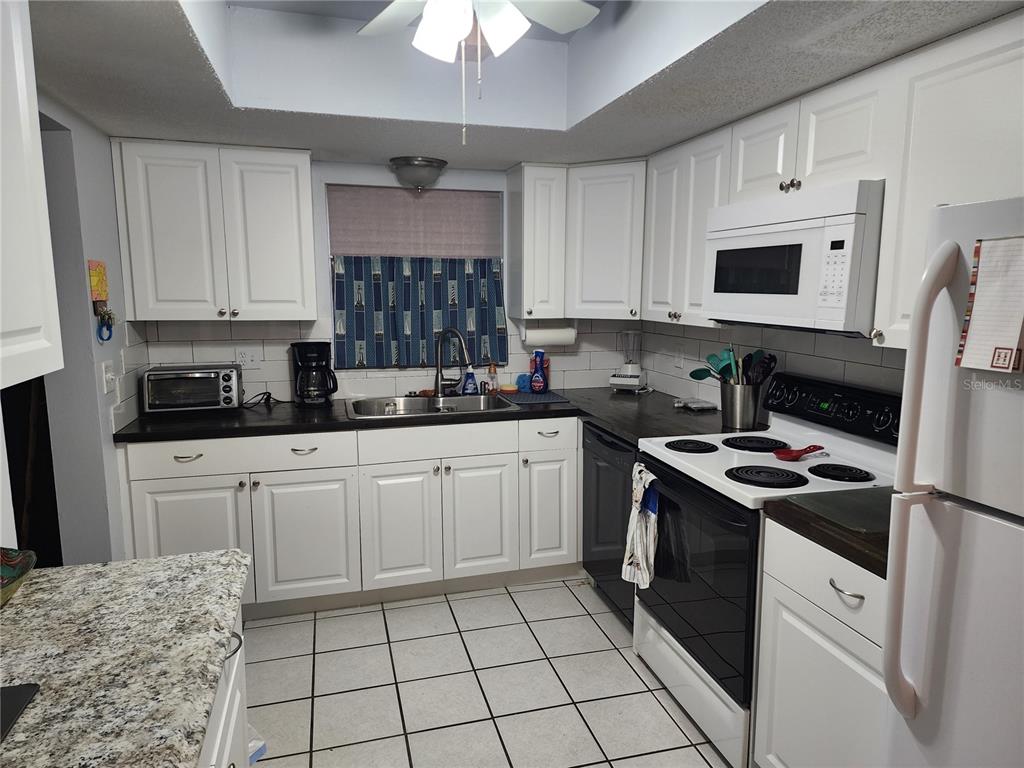 A kitchen features white cabinets, black countertops, a white stove, and tiled flooring — 3064 LAKE BAYSHORE DRIVE UNIT 115, BRADENTON, FL