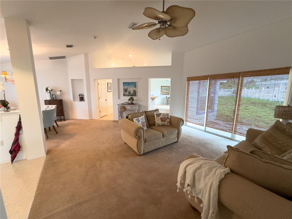 A carpeted living room features a ceiling fan, beige sofas, and large windows with blinds — 13076 SW 78TH TERRACE, OCALA, FL