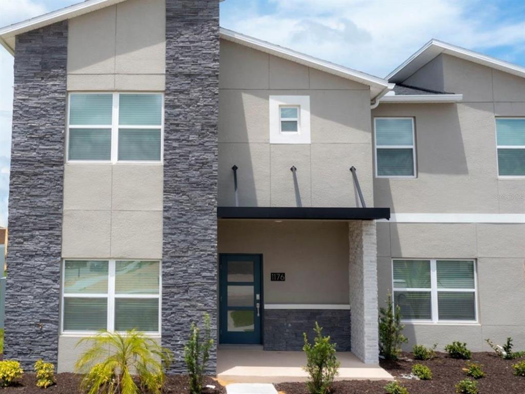 A two-story townhouse exterior features gray stucco, stone accents, and a modern front door — 1176 CHALLENGE DRIVE, DAVENPORT, FL