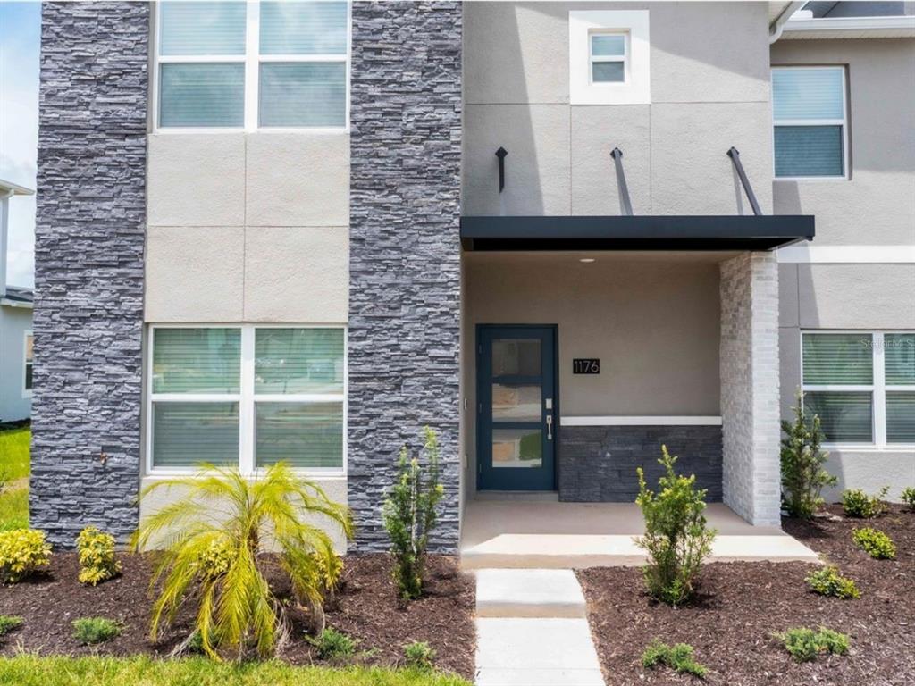 The exterior of a two-story home features gray stone accents, a dark blue door, and landscaping — 1176 CHALLENGE DRIVE, DAVENPORT, FL