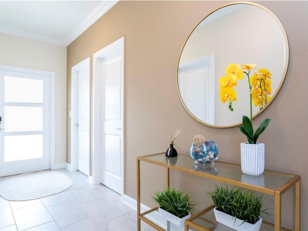 A modern entryway features a glass console table, a round gold mirror, and potted plants — 1176 CHALLENGE DRIVE, DAVENPORT, FL