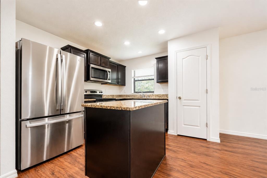 A kitchen features dark wood cabinets, granite countertops, stainless steel appliances, and wood-look flooring — 706 W CHELSEA STREET, DELAND, FL
