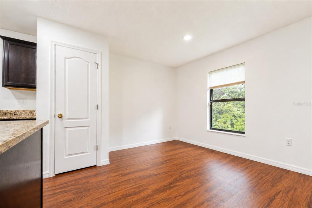 An empty room with wood-look flooring, a white door, and a window overlooking trees — 706 W CHELSEA STREET, DELAND, FL