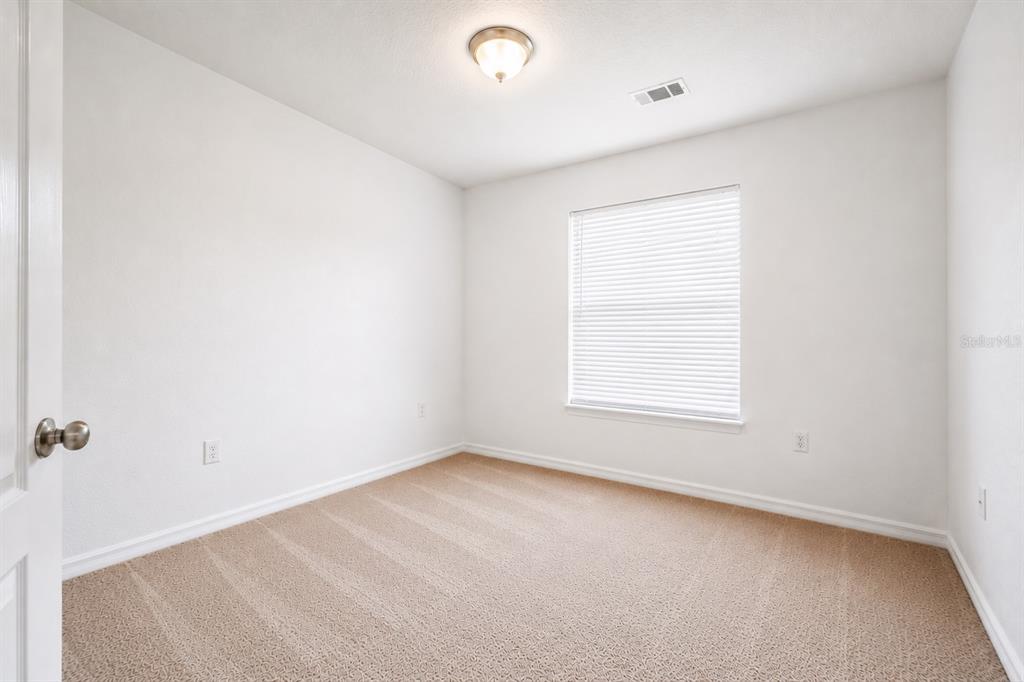 An empty bedroom features beige carpet, white walls, a single window with blinds, and lighting — 706 W CHELSEA STREET, DELAND, FL