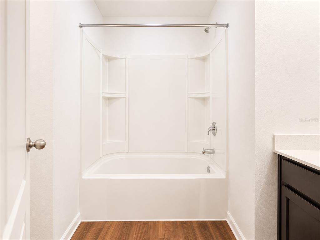 A bathroom features a white bathtub with a shower surround and a dark vanity cabinet — 706 W CHELSEA STREET, DELAND, FL