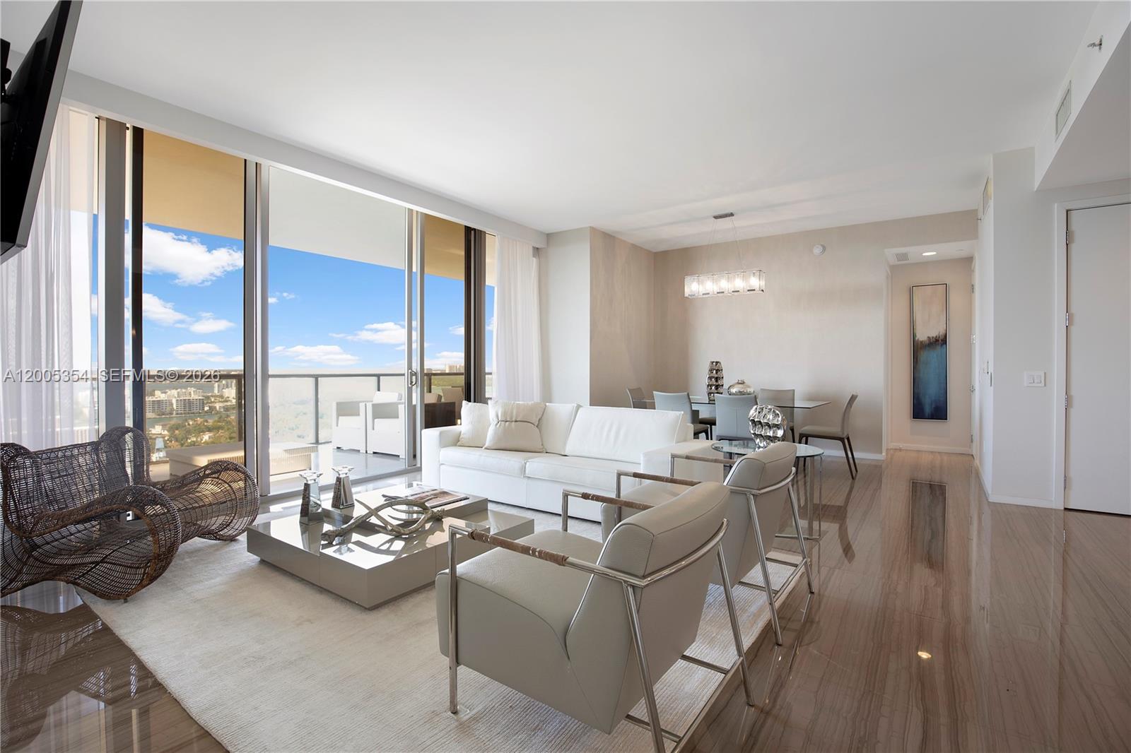 A modern living room features white furniture, a glass coffee table, and a balcony view — 9705 Collins Ave # 1805N, Bal Harbour FL 33154, BAL HARBOUR, FL