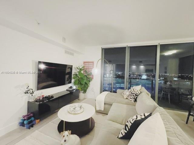 A modern living room features a large sectional sofa, a television, and floor-to-ceiling windows — 121 NE 34th St # 1409, Miami FL 33137, MIAMI, FL