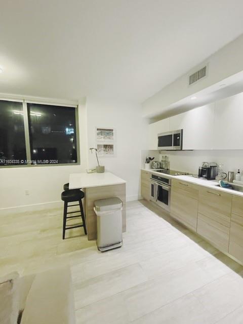 A modern kitchen features light wood cabinetry, white countertops, and a small breakfast bar — 121 NE 34th St # 1409, Miami FL 33137, MIAMI, FL