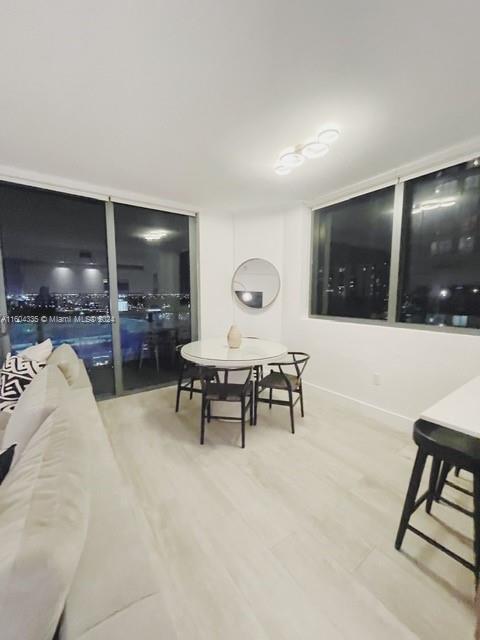 A modern dining area with a round table and chairs sits beside floor-to-ceiling windows — 121 NE 34th St # 1409, Miami FL 33137, MIAMI, FL