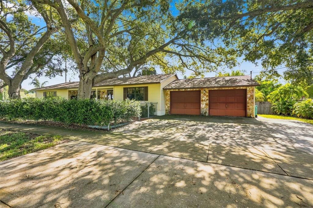 A single-story house with yellow siding, a two-car garage, and large trees in the yard — 617 MEHLENBACHER ROAD, LARGO, FL