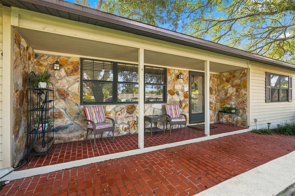 A covered brick porch features stone walls, two chairs, and a small table — 617 MEHLENBACHER ROAD, LARGO, FL