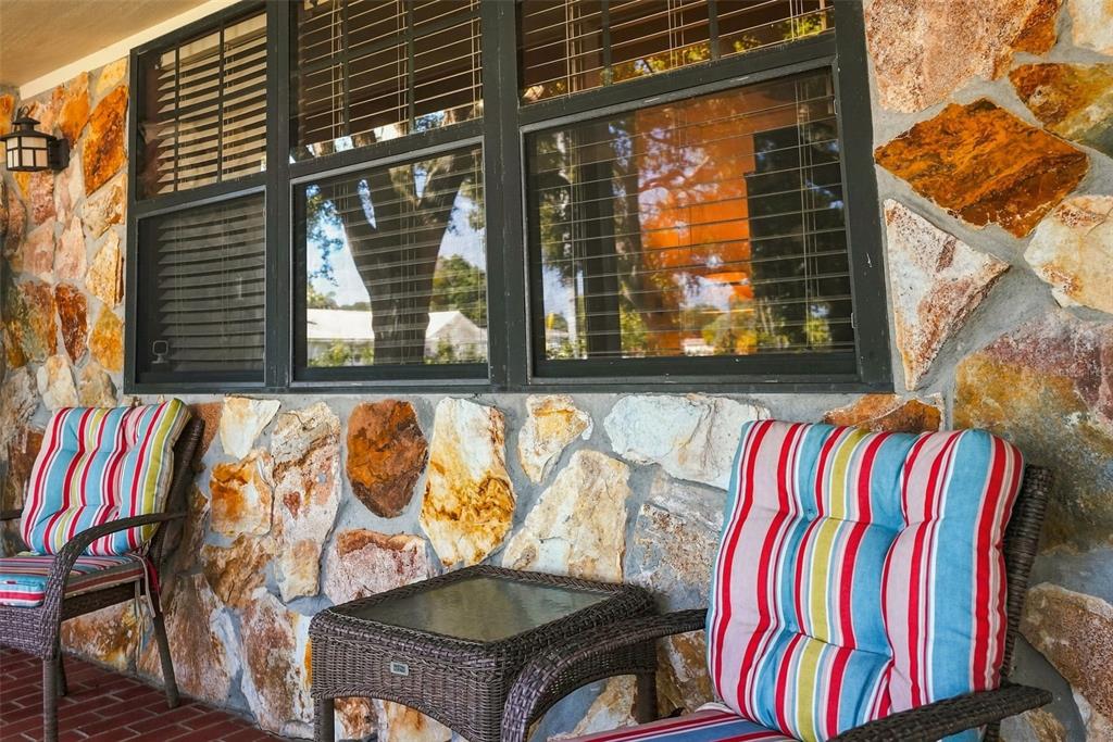 A stone-walled porch features two wicker chairs with striped cushions and a small glass table — 617 MEHLENBACHER ROAD, LARGO, FL