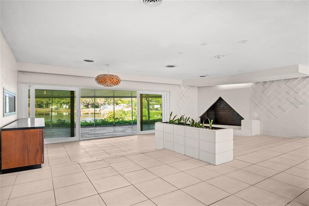A spacious living room features light tile flooring, a geometric fireplace, and sliding glass doors — 801 PINELLAS POINT DRIVE S, ST PETERSBURG, FL