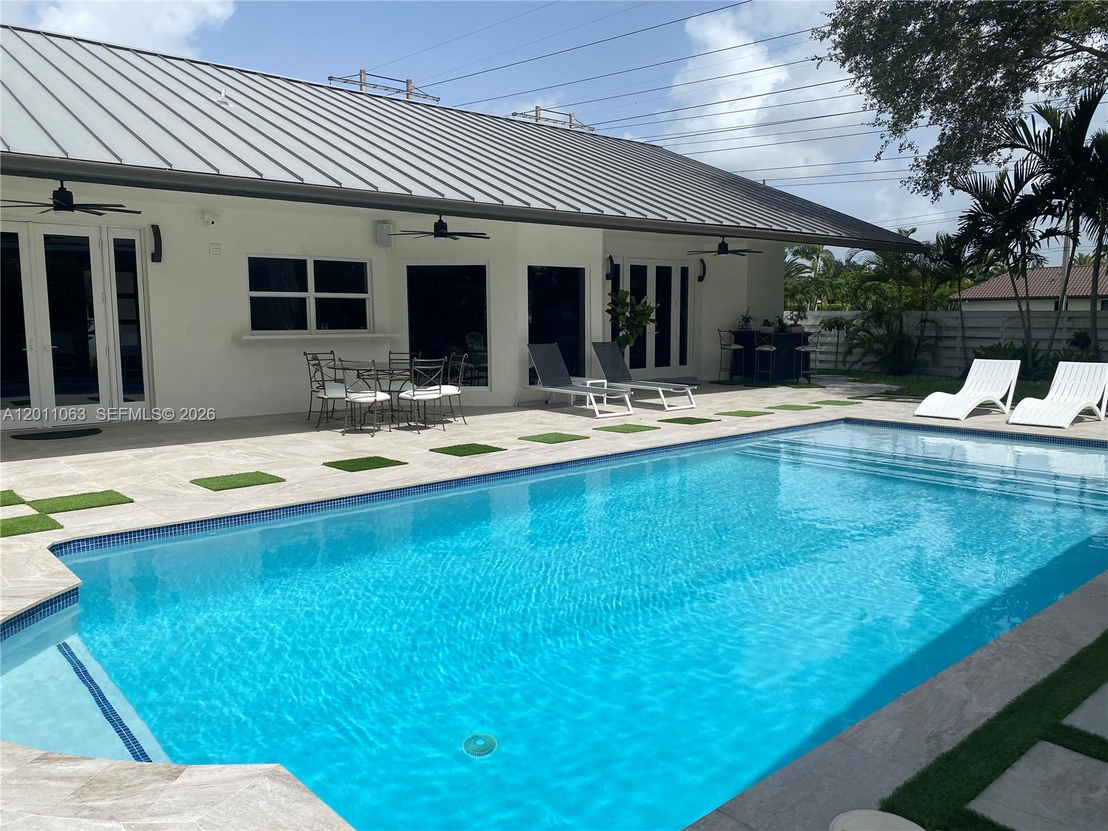 A swimming pool sits on a patio next to a white house with a metal roof — 13255 SW 106th Ave, Miami FL 33176, MIAMI, FL