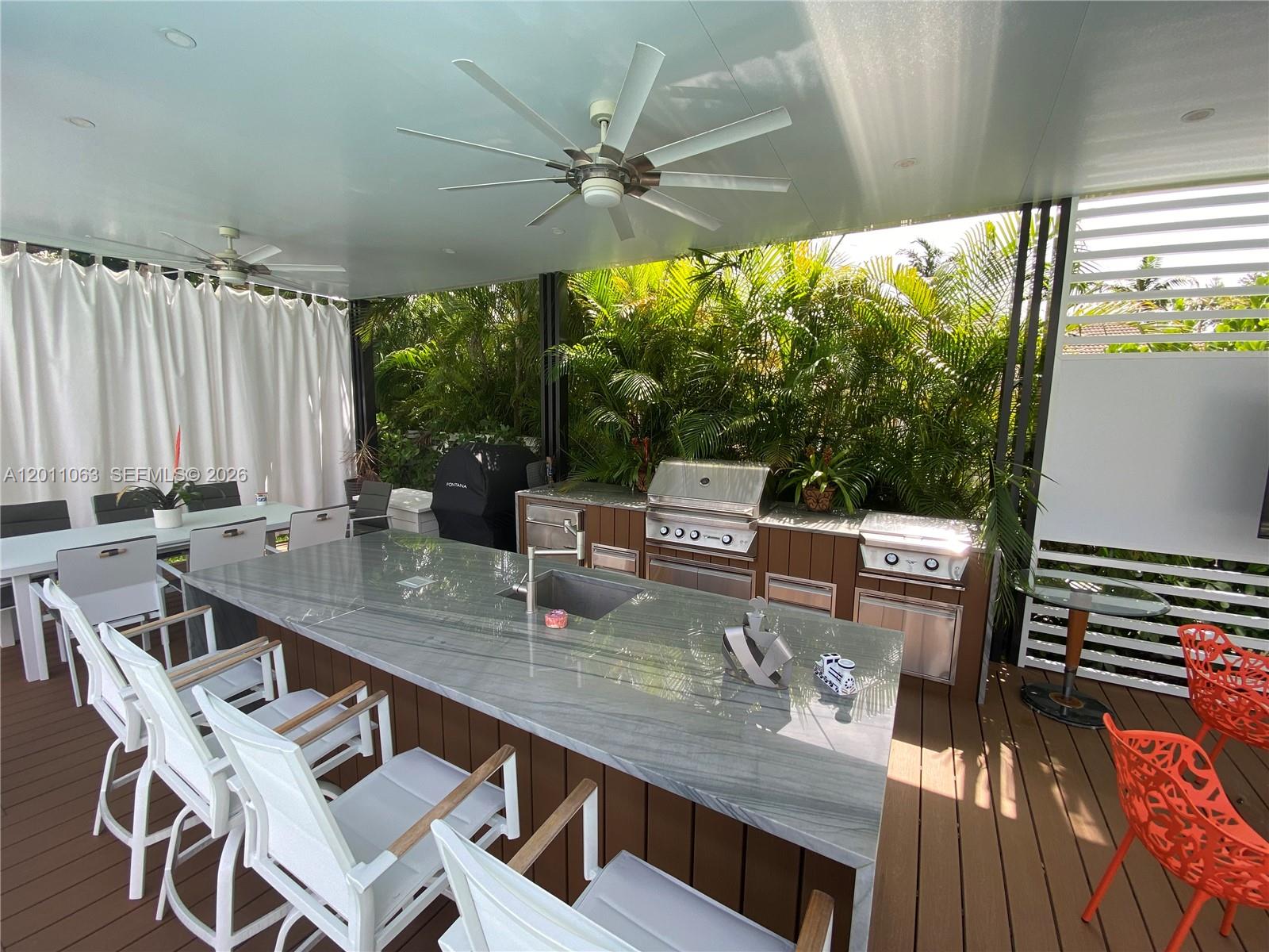 An outdoor kitchen features a large stone island with a sink and stainless steel appliances — 13255 SW 106th Ave, Miami FL 33176, MIAMI, FL