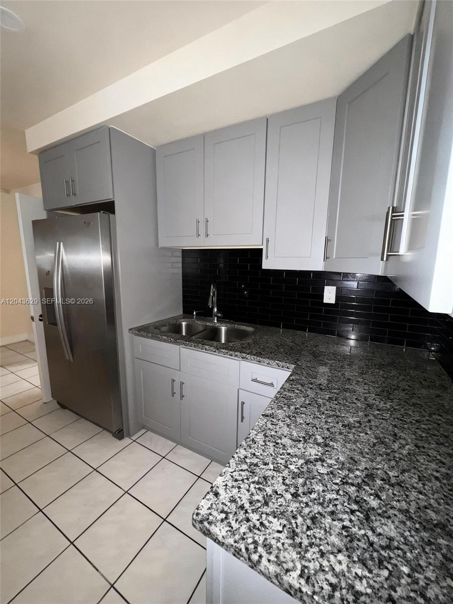 A kitchen features grey cabinets, granite countertops, a stainless steel refrigerator, and a black backsplash — 5912 Fillmore St # 2, Hollywood FL 33021, HOLLYWOOD, FL