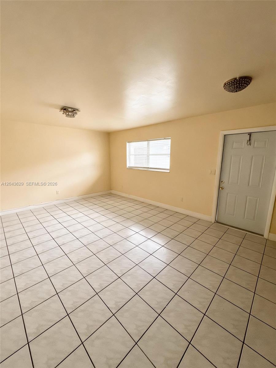 An empty room features light-colored walls, a tiled floor, a window, and two ceiling lights — 5912 Fillmore St # 2, Hollywood FL 33021, HOLLYWOOD, FL
