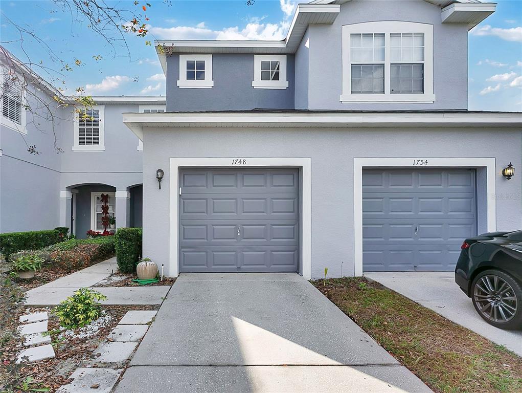 A two-story townhouse exterior features two gray garage doors and a concrete driveway — 1748 FRITWELL COURT, OCOEE, FL