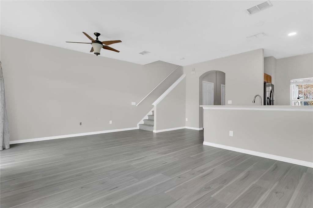 A living room with gray wood-look flooring, a ceiling fan, and stairs leading upward — 1748 FRITWELL COURT, OCOEE, FL