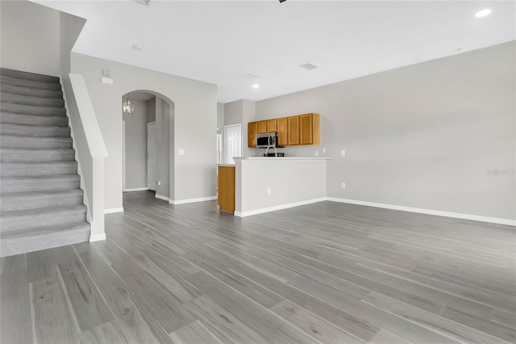 An open-concept living area features gray wood-look flooring, a staircase, and a kitchen with cabinets — 1748 FRITWELL COURT, OCOEE, FL