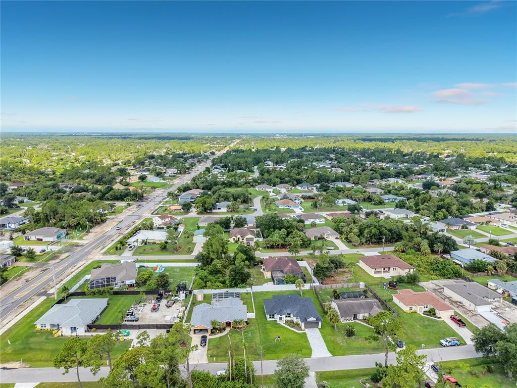 An aerial view shows a suburban neighborhood with houses, green lawns, and a main road — 1081 MCCRORY STREET, NORTH PORT, FL